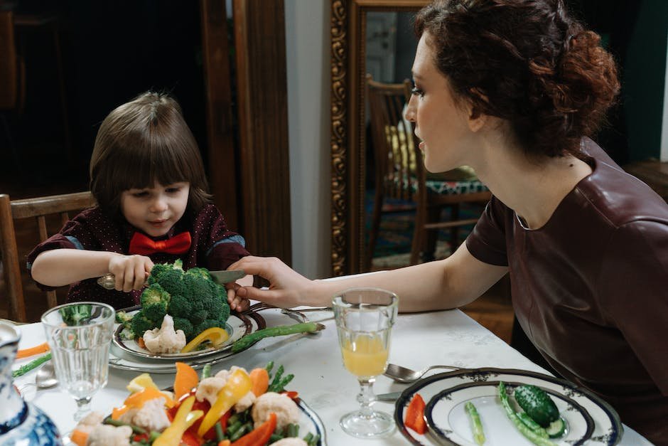 A child with Autism Spectrum Disorder sitting at a table and looking at a plate of broccoli with an apprehensive expression on their face.