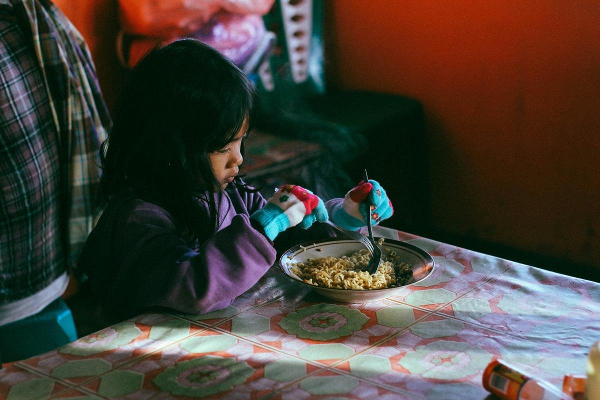 In this image, a child is sitting at a table and looking hesitant while holding a spoon, depicting the challenges that can arise during mealtimes for children with feeding issues.