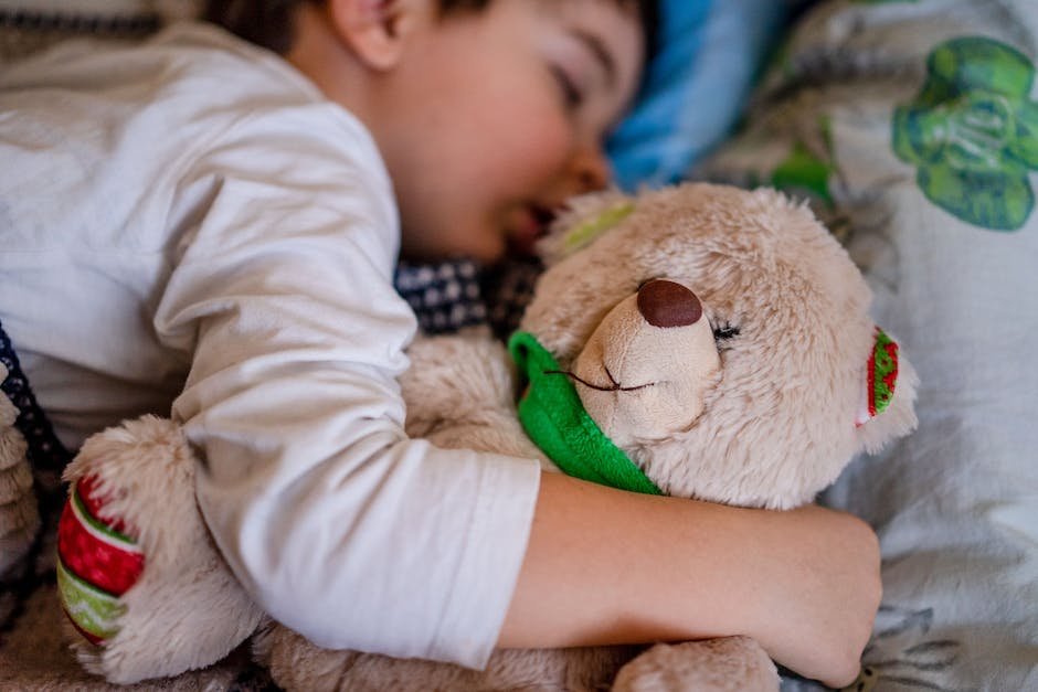 An image of a child sleeping peacefully with a teddy bear beside them